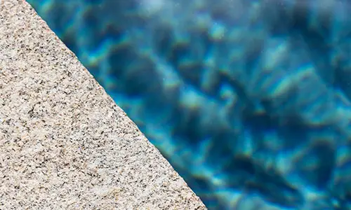 Gros plan sur margelle en granit clair bordant une piscine.