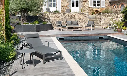 Mobilier de détente au bord d’une piscine moderne dans un jardin paysager.