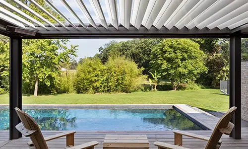 Vue d’une piscine avec terrasse et pergola bioclimatique installée par Nymfeo, donnant sur un grand jardin arboré